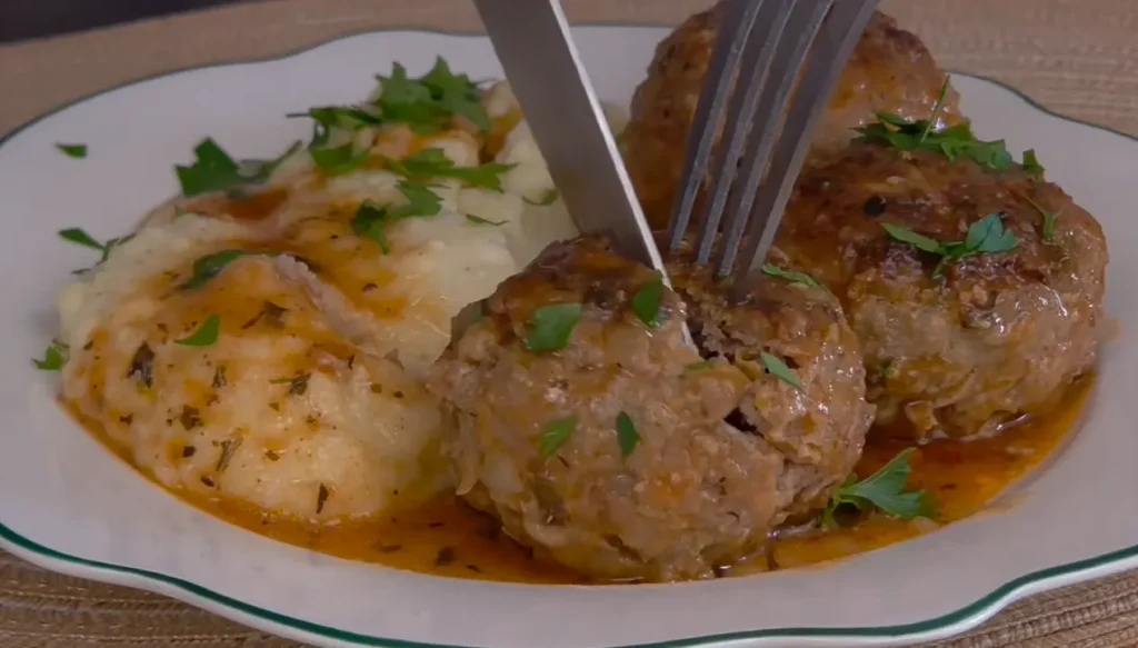 Juicy beef meatballs in spicy tomato sauce served with creamy mashed potatoes and fresh parsley.