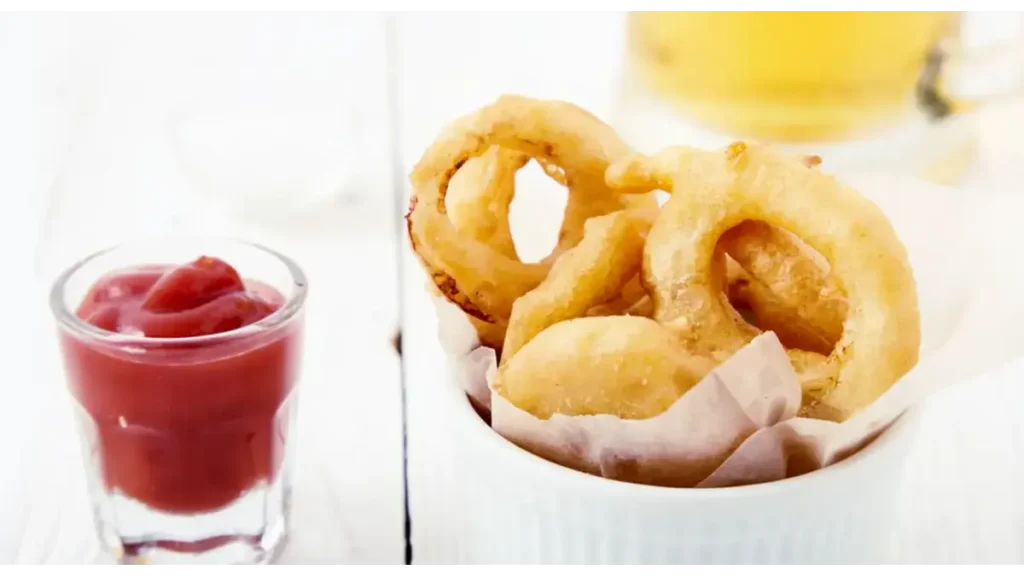 Golden crispy onion rings topped with melted cheddar cheese on a serving plate.