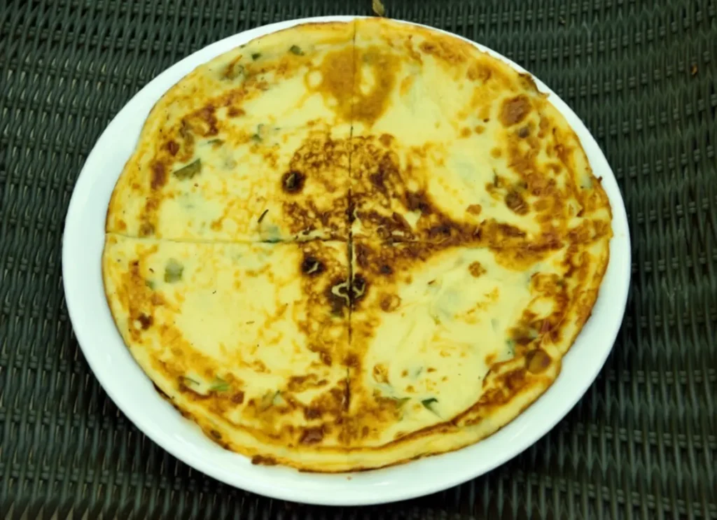 Golden kaygana folded on a white plate with chopped parsley and spring onions